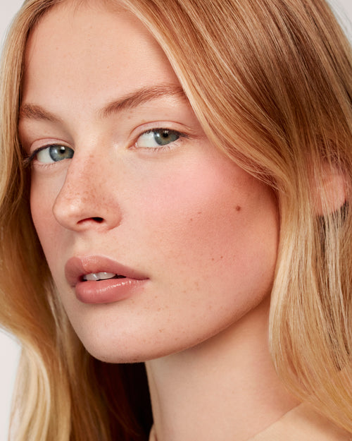 Blonde model wears the Baby Cheeks Powder Blush Duo in Coquette / Mimi. 